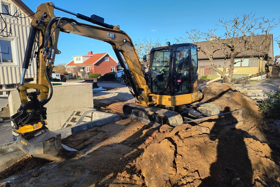 Grävmaskin i trädgård.